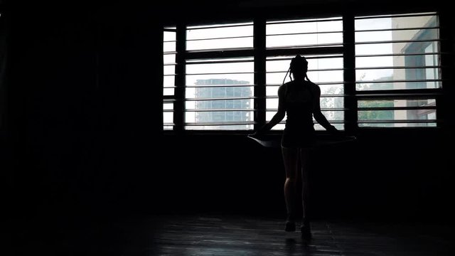 silhouette panning female boxer in wrapped bandage hands jumping on skipping rope in gym. Fit woman preparing to boxing competition. Wellness, fighting, motivation, martial arts, self defense concept