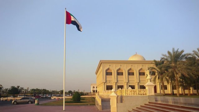 The United arab emirates flag waving in Sharjah city at sunset
