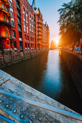 Touristic spot old red brick illuminated buildings, canal and square in golden sunset light. Speicherstadt Hamburg. Warehause District at dawn