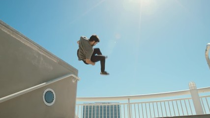 Slow motion parkour athlete in urban city doing extreme front flip off ledge with lens flare  - Powered by Adobe
