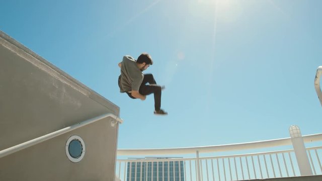 Slow motion parkour athlete in urban city doing extreme front flip off ledge with lens flare 