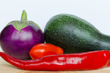 The eggplant, zucchini, tomatoe and a pepper on the wooden table