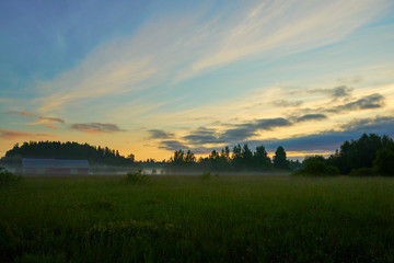 Foggy sunrise on a field with cloudy sky.