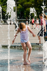A litlle boy is playing near the fountain in the summer