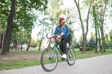 Young happy girl in stylish clothes rides a green bike in the park. Student girl is actively resting in a park on a bicycle. Walk on the bike. Woman rides a bike in the park.