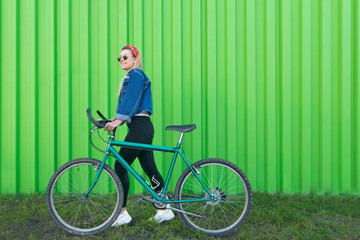 Portrait of a stylish woman in full length pulling a bicycle on the background of a green wall. Teen girl walking with a bicycle on a green background. Copyspace