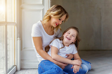 Mother hugging child. Woman and girl relax and playing in bedroom near windiow. Happy family at home. Mom playing with her daughter. Family, maternity, tenderness, parenthood, responsibility concept