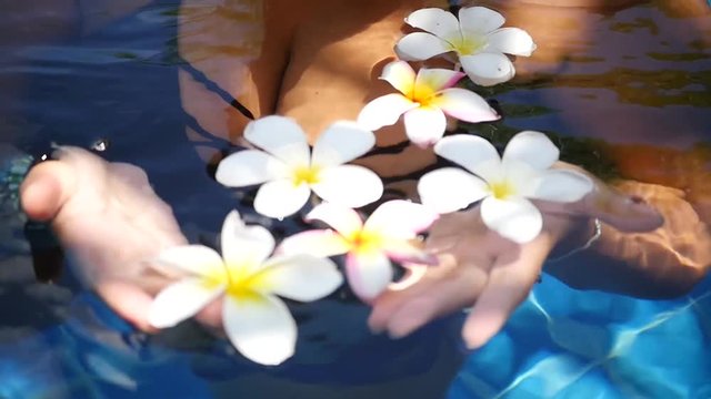 Sexy girl with big breasts floating in a blue pool among the beautiful flowers. slow motion, HD, 1920x1080