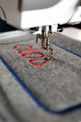 closeup on grey felt with red lettering stitched by a modern computerised sewing machine with...