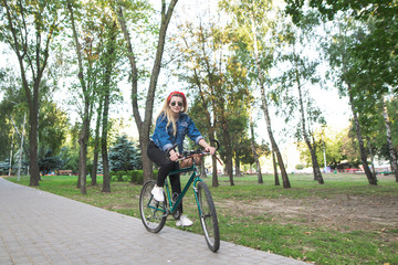 Young girl in stylish clothes and sunglasses rides a green bike in the park. Walk on the bike. Active leisure concept