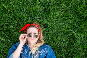 Portrait of an attractive stylish girl in a denim jacket lying on a green lawn, looking into the...