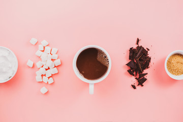 Flatlay of vegan cocoa, chocolate, coconut cream, sugar and vegetarian marshmallows on pink