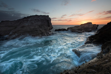 Fototapeta na wymiar A long exposure of blurred waves swirling and crashing over rugged rocks on the rocky Cornish coastline in Cornwall, UK.