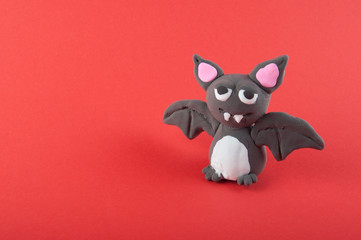 Funny grey bat made of modelling clay staying on red background. Copy space for text