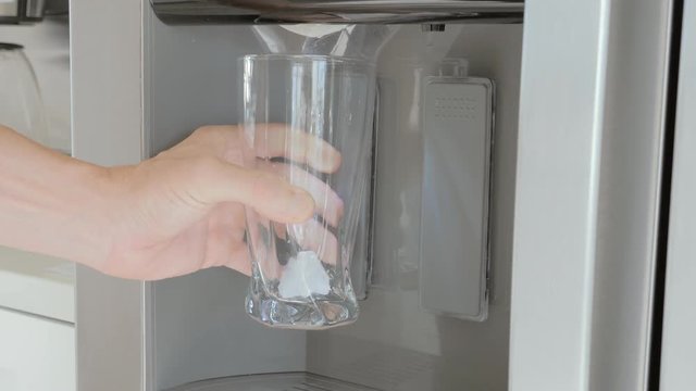 A man pours ice cubes from a fridge door into a glass