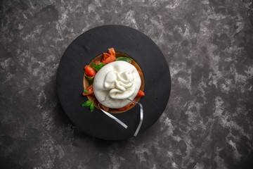 Whole tied Italian cheese burrata on small wooden plate served with fresh tomatoes and basil on dark textured background © Eduard Zhukov