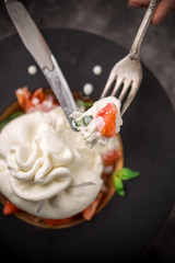 Whole tied Italian cheese burrata on small wooden plate served with fresh tomatoes and basil on dark textured background © Eduard Zhukov