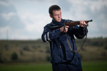 Young police officer in uniform, with weapon in hand on rural landscape background