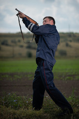 Young police officer in uniform, with weapon in hand on rural landscape background