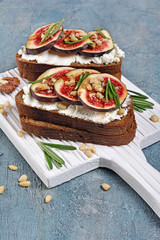 Vegetarian sandwich with figs, soft cheese, honey, nut and rosemary on white wooden board