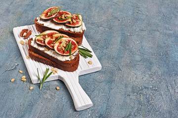 Vegetarian sandwich with figs, soft cheese, honey, nut and rosemary on white wooden board