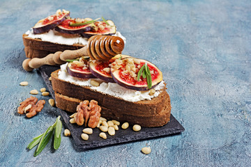 Vegetarian sandwich with figs, soft cheese, honey, nut and rosemary on black slate board