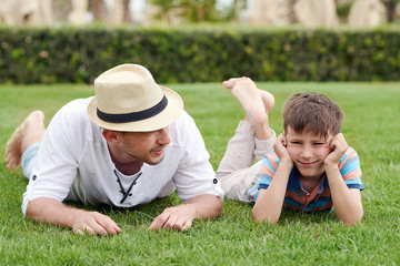 European man is laying at the hotels lawn with his cute son. They are talking and having a rest.