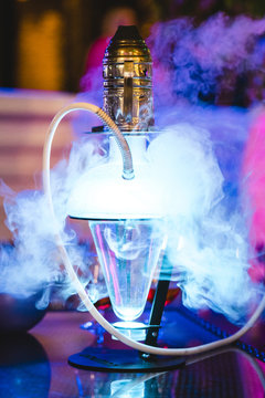 Close up of illuminated hookah with smoke on table in nightclub