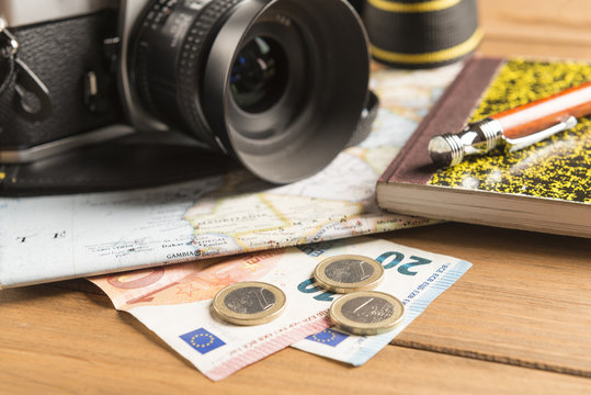 Camera, map, notebook, ball pen and money on wooden table