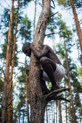 Male black with no shirt climbs a tree