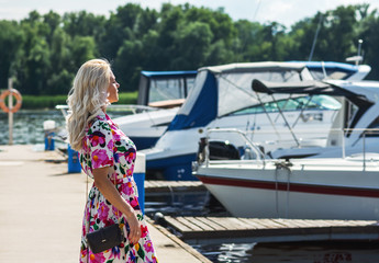 Fototapeta na wymiar Beautiful girl in a dress is stand on the pier against the backdrop of yachts in summer