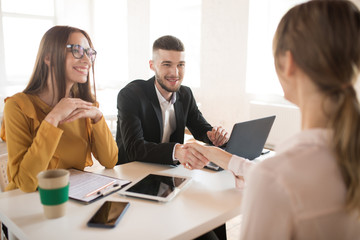 Cheerful business man with laptop and business woman in eyeglasses happily talking with applicant about work. Young employers spending job interview in office