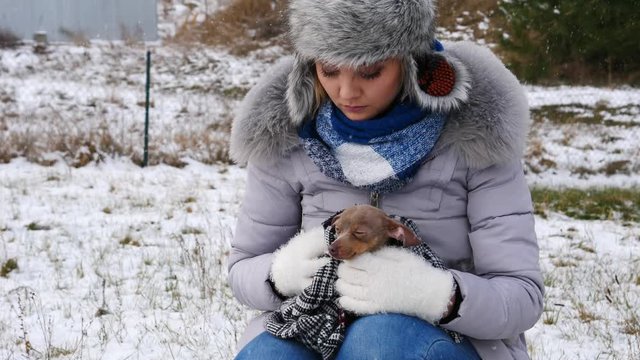 Young worried woman taking care of her little dog pinscher ratter prazsky krysarik feeling cold during winter.