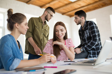 Two pretty girls working together in modern office with colleagues on background. Group of creative people spending time at work
