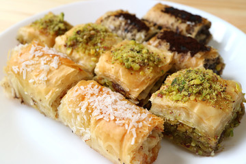 Different types of mouthwatering Baklava pastries served on white plate, selective focus and blurred background 