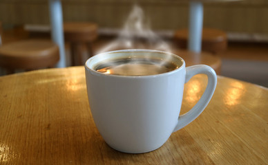One cup of hot coffee with smoke on round wooden table, blurred background 