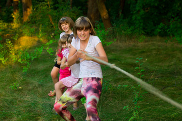 Group of happy children playing tug of war outside on grass. Kids pulling rope at park. Summer camp...