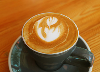 Closed Up Hot Cappuccino Coffee with Latte Art in a Dark Grey Cup Served on Wooden Table 