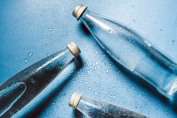 A glass bottle of water on blue background splashes drops of water on top. Quench thirst....