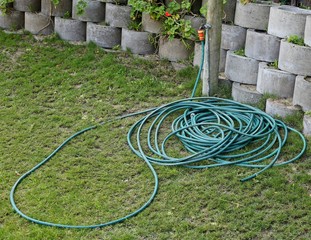 A tap connected to a green hose pipe. A gardening or water conservation concept image. 