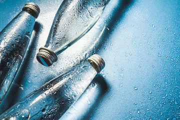 A glass bottle of water on blue background splashes drops of water on top. Quench thirst....