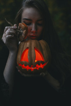 Young woman looking at illuminated jack o lantern in forest during Halloween