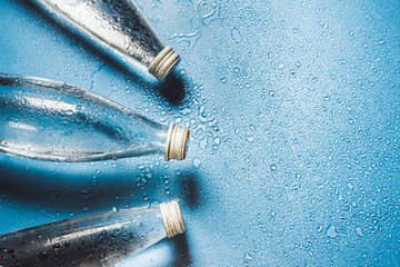 A glass bottle of water on blue background splashes drops of water on top. Quench thirst....