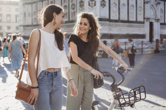 Female friends with bicycle talking while walking on city street against Florence Cathedral