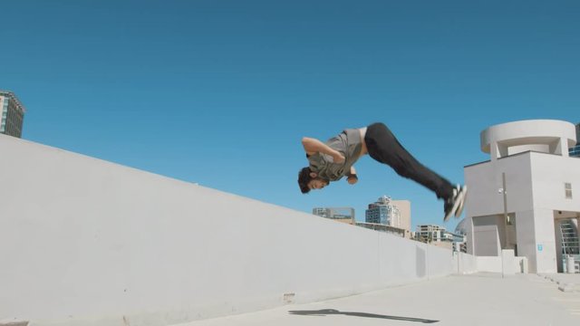 Slow motion parkour athlete doing extreme backflip off wall in urban city outside isolated in sky