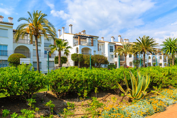Holiday apartments in tropical garden on sea coast promenade near Estepona town on Costa del Sol, Spain - obrazy, fototapety, plakaty