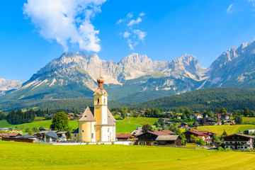 Church on green meadow in Going am Wilden Kaiser mountain village on sunny summer day, Tyrol, Austria - obrazy, fototapety, plakaty