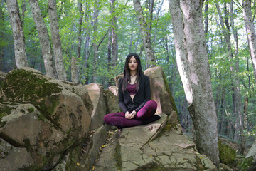 Naklejka na ściany i meble Yogi girl meditating on rock in the forest