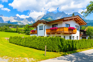 Typical wooden alpine house decorated with flowers on green meadow in Going am Wilden Kaiser village on sunny summer day, Tyrol, Austria