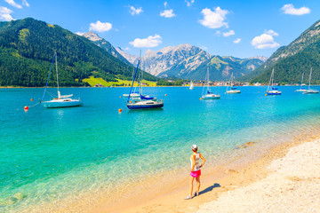 Fototapeta na wymiar Young woman tourist standing on beautiful Achensee lake beach on sunny summer day, Tirol, Austria